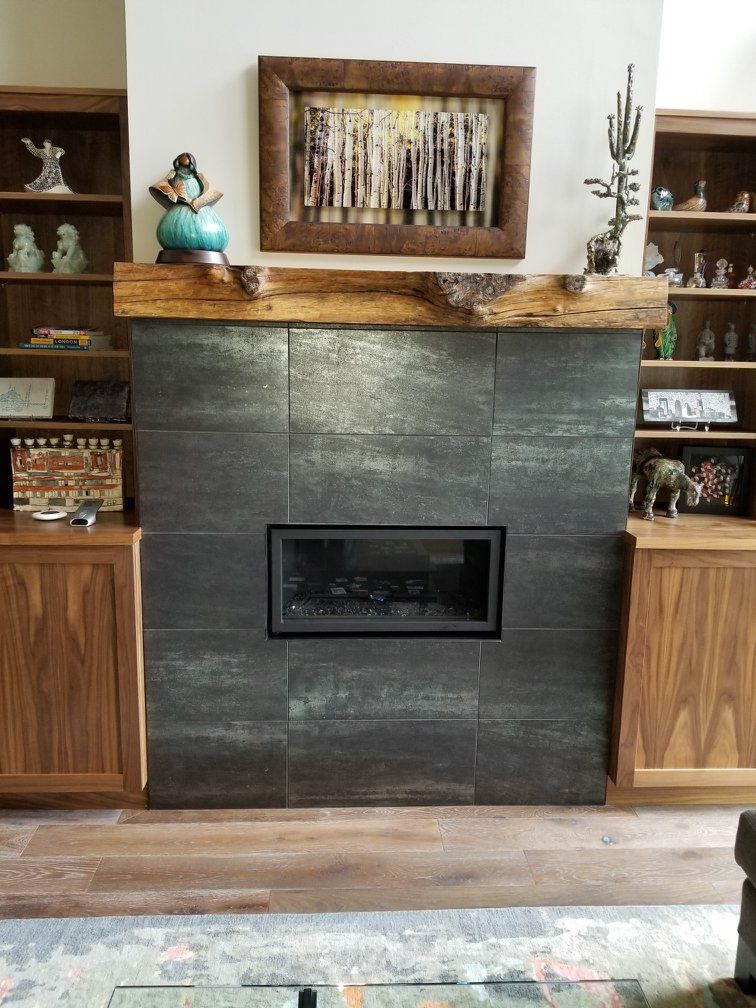 Hardwood flooring in front of a fireplace with dark tile surround and wooden built-in cabinets.