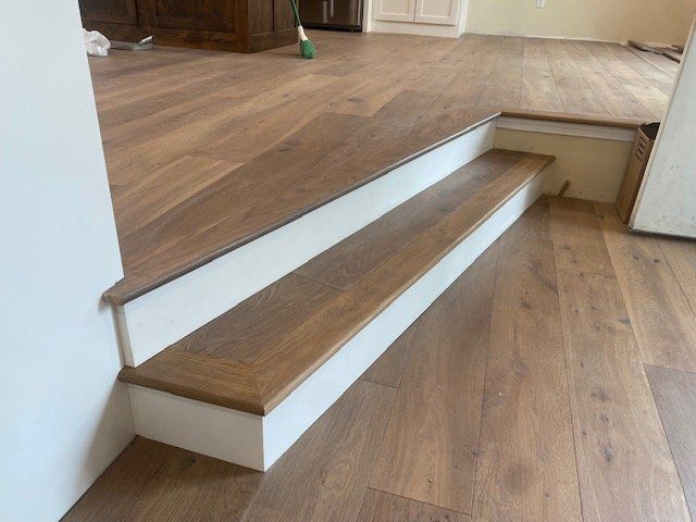 Hardwood planks installed on stair treads with white painted risers and stringers in a residential hallway.