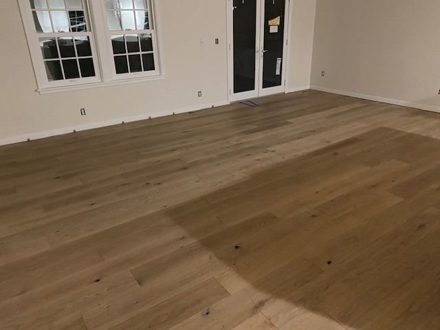 Medium-toned hardwood plank flooring in an empty room with windows and doors visible.