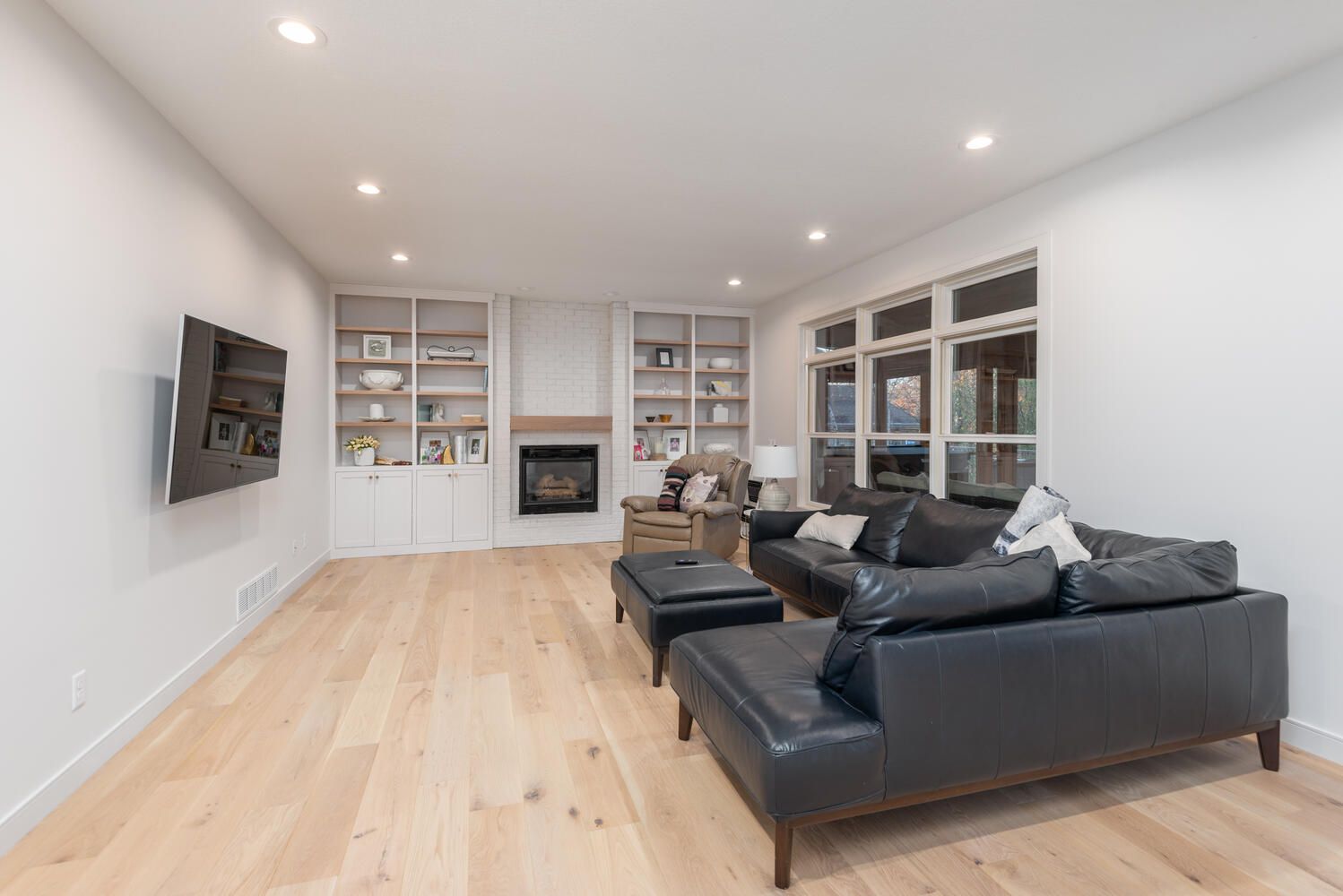 Light-toned hardwood plank flooring in a living room with built-in cabinetry, fireplace, and black leather seating.