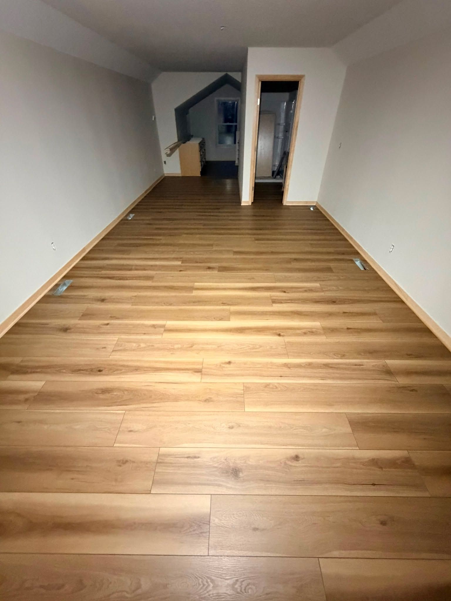 Newly installed medium brown wood-look LVP planks in a basement room with white walls and a doorway visible at the far end.