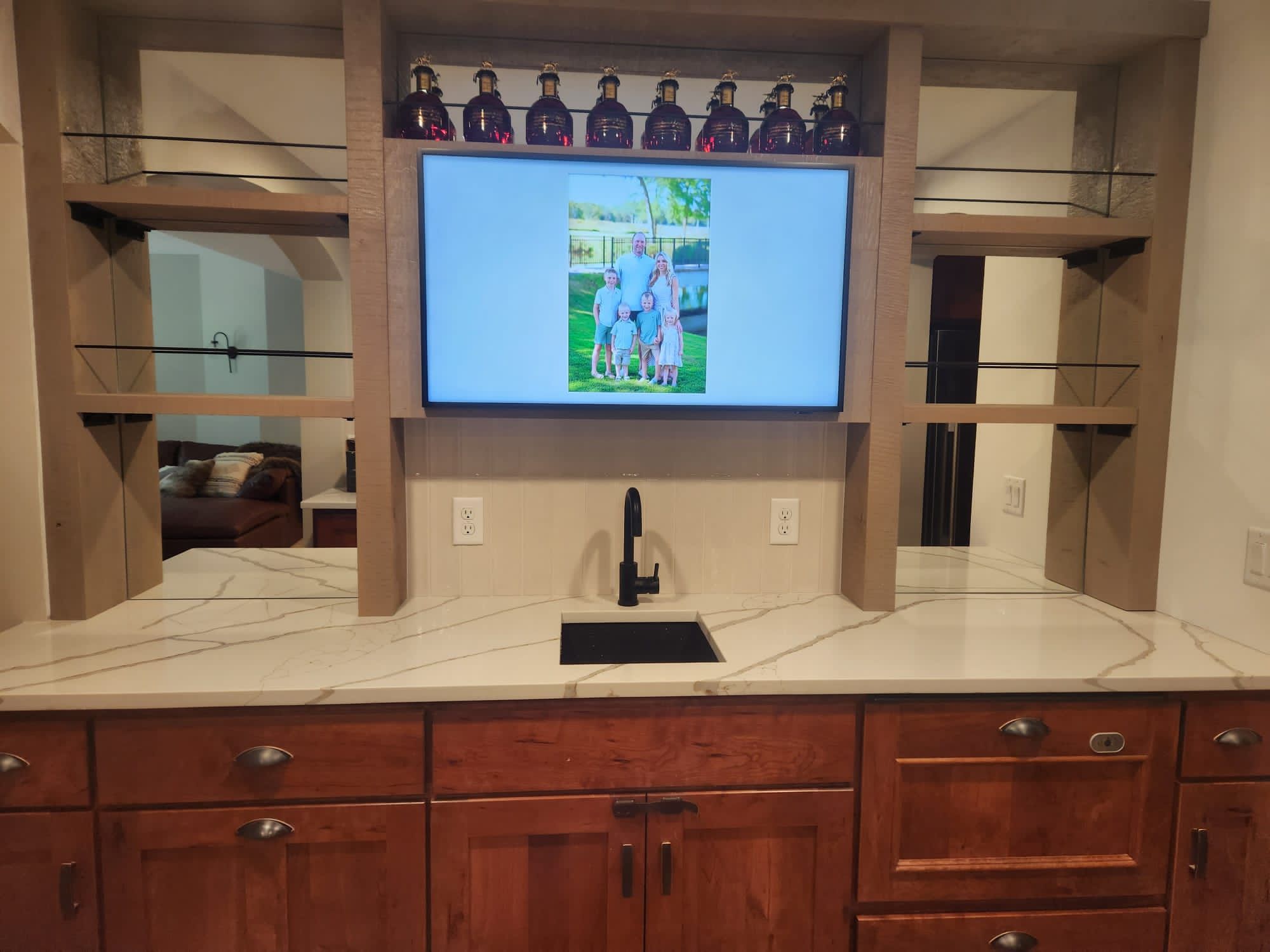 Light colored tile backsplash installed above a kitchen sink with integrated media display.