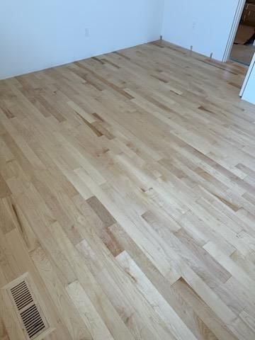 Newly installed light maple hardwood plank flooring in a living room.