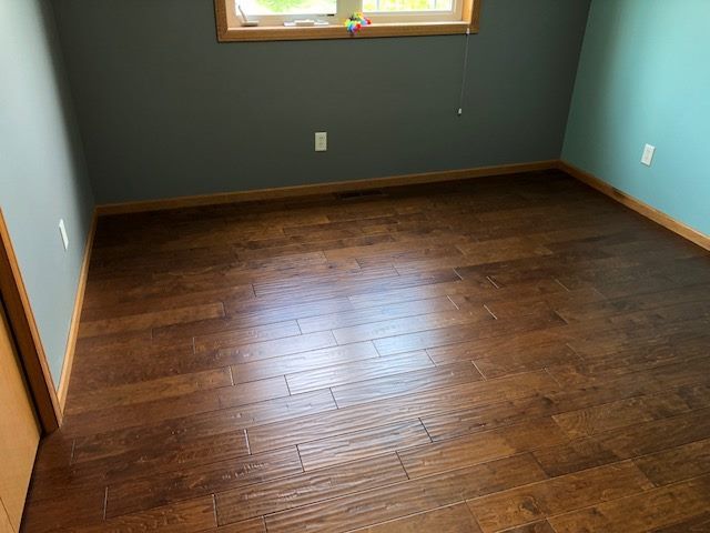 Newly installed medium brown hardwood plank flooring in a bedroom with wood baseboard trim.