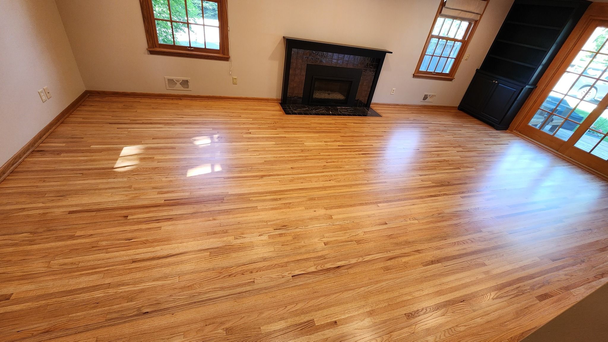 Refinished hardwood plank flooring in a living room with a fireplace and windows.