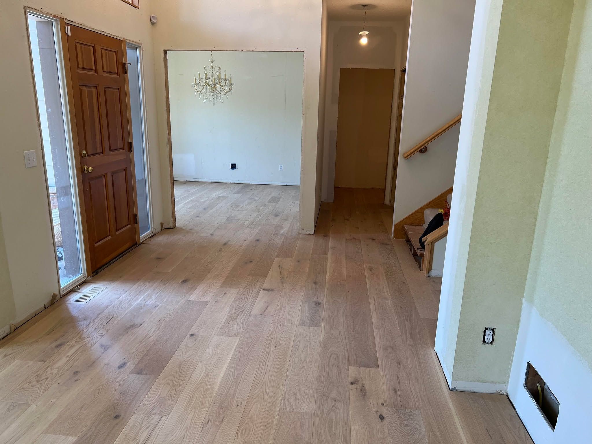 Light-finish engineered white oak plank flooring in an open living space with stairs and wood trim.