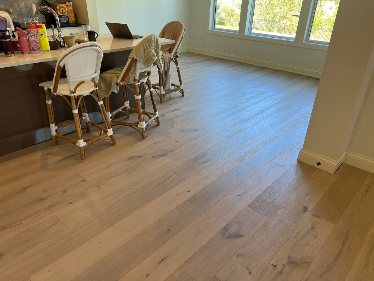 Medium-toned engineered hardwood plank flooring installed in a living space with kitchen counter and seating areas visible.