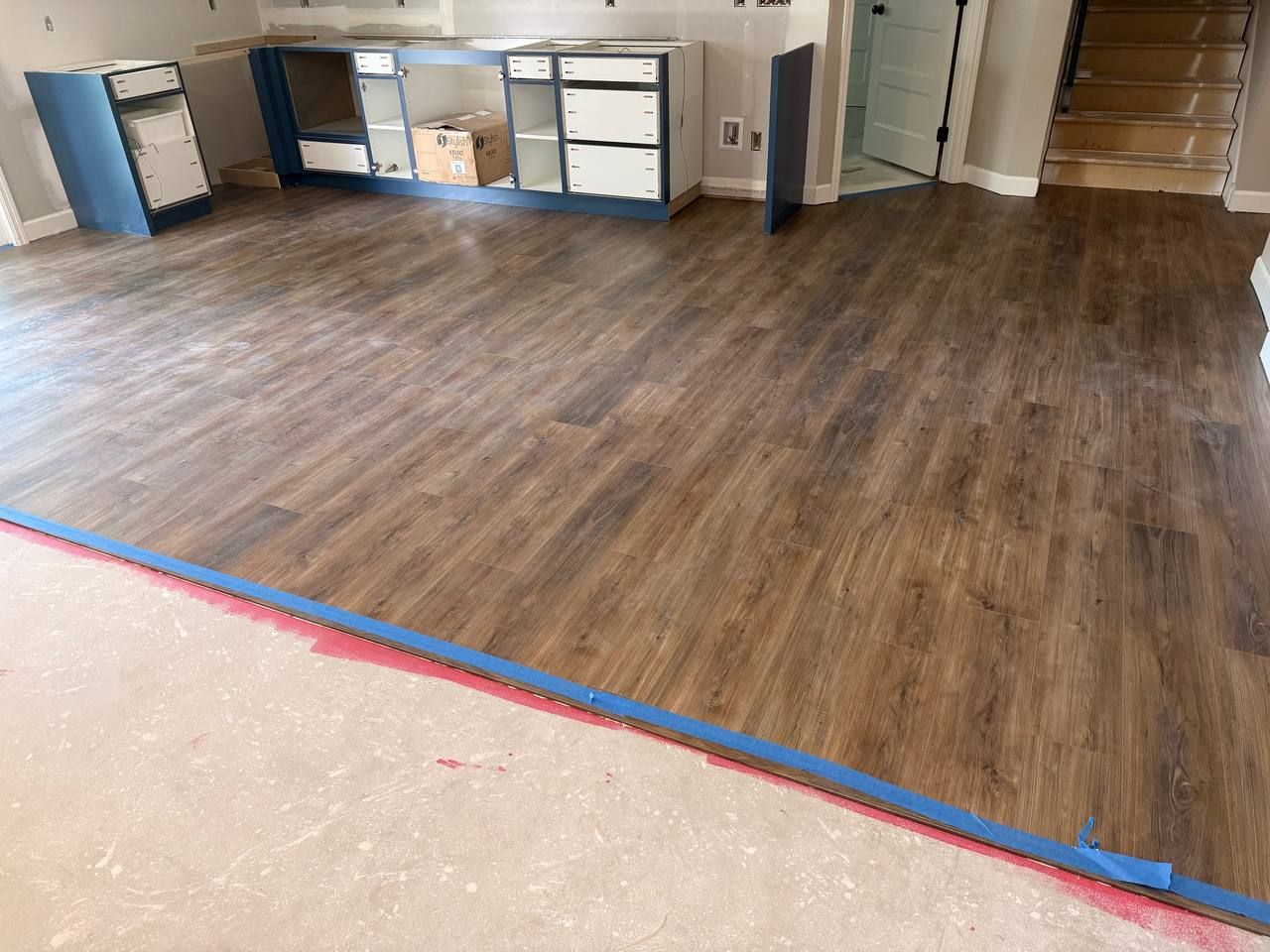 Luxury vinyl plank flooring in brown wood tones installed in a large open room with concrete subfloor visible at the edge.